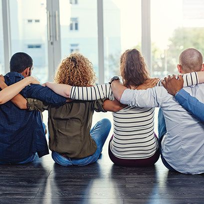 Students sitting on the floor with their arms over each other's shoulders. Gifts of Real Estate