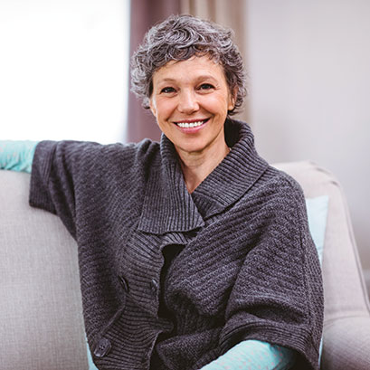 A woman sitting on a couch, smiling. Gifts of Life Insurance